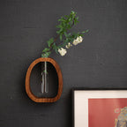 Wooden wall shelf with a glass vase containing greenery and white flowers against a dark gray wall.