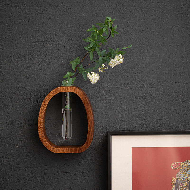 Wooden wall shelf with a glass vase containing greenery and white flowers against a dark gray wall.
