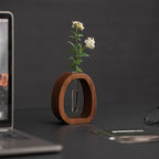 Wooden vase with a plant on a desk next to a laptop and smartphone.