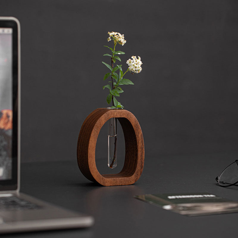 Wooden vase with a plant on a desk next to a laptop and smartphone.