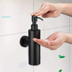 A matte black wall-mounted pump dispenser being used by two hands to dispense soap onto a palm, set against a light gray tiled wall.