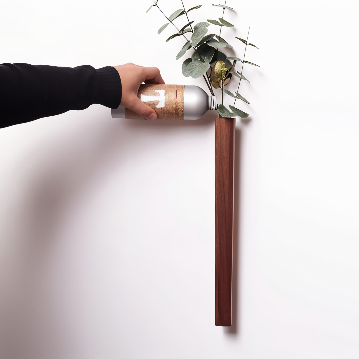 Person holding a bottle against a white wall with a plant on a stand.