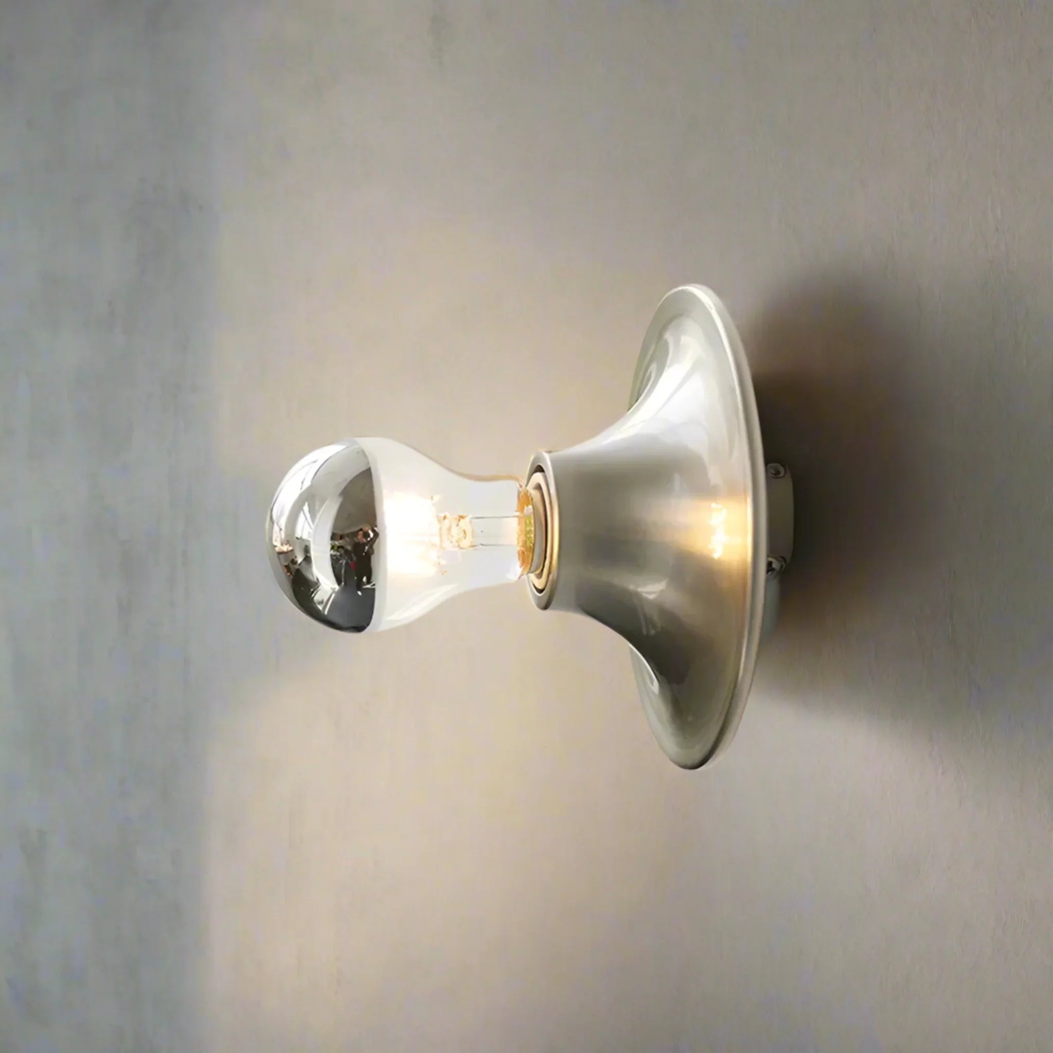 Wall-mounted light fixture with a clear glass shade on a neutral background