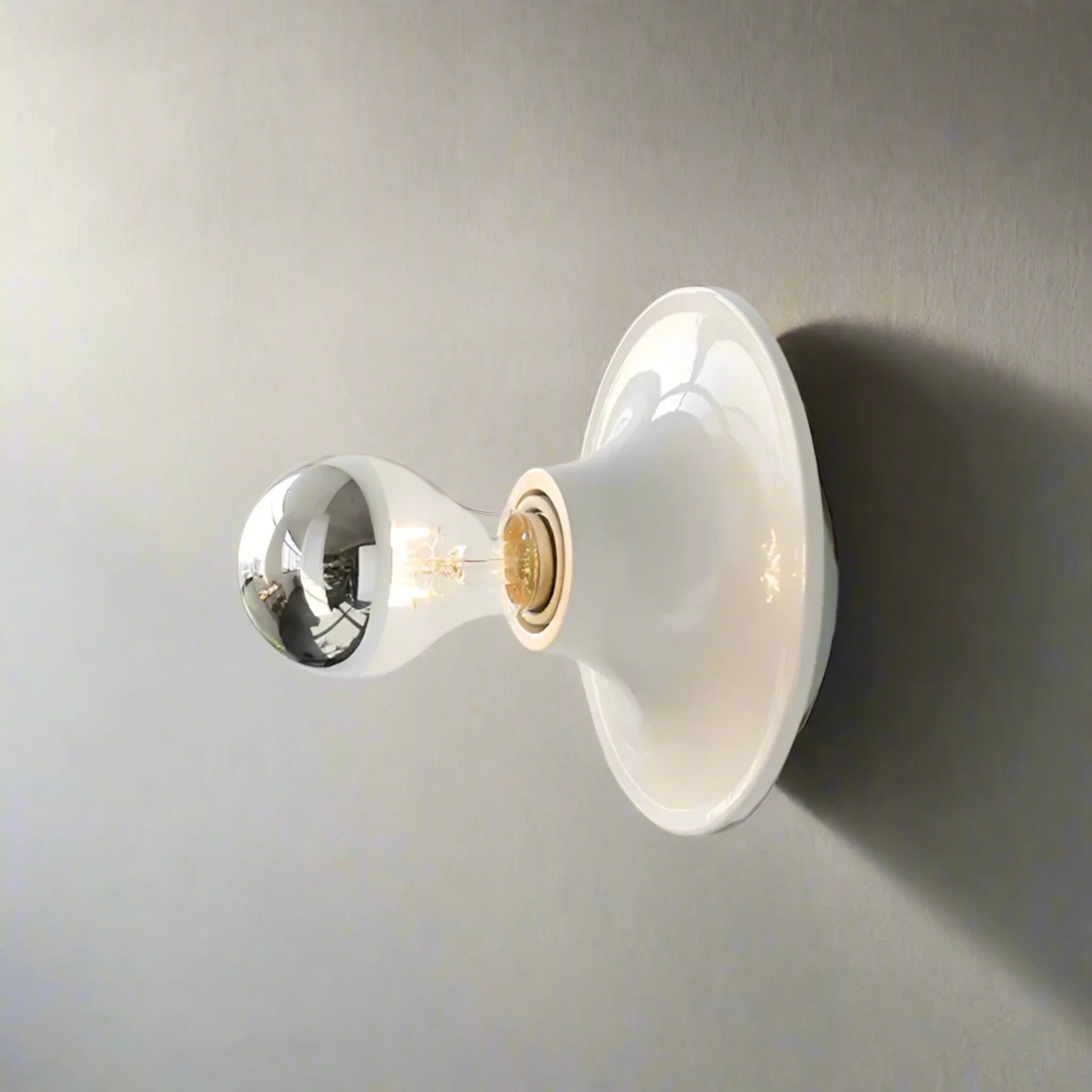 Wall-mounted light fixture with a white glass shade on a gray background