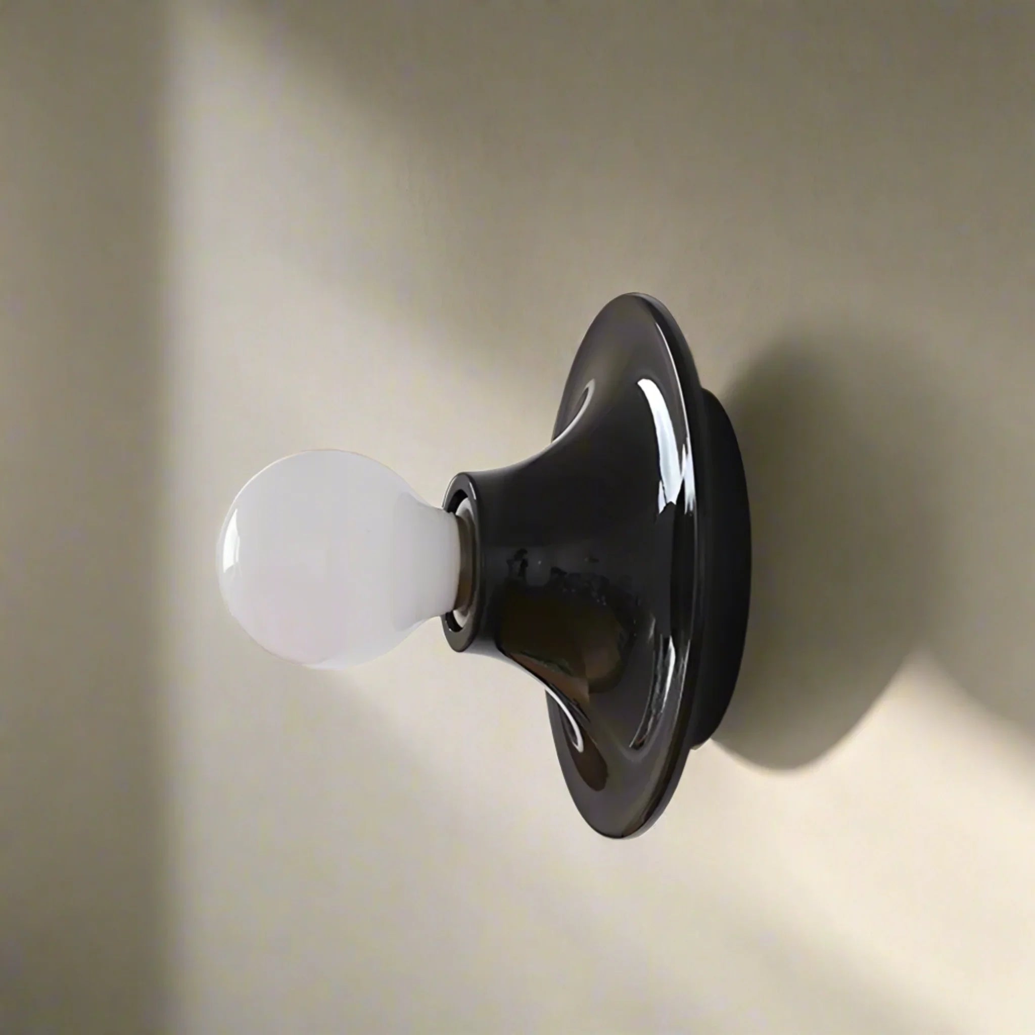 Black wall-mounted light fixture with a white bulb on a beige background