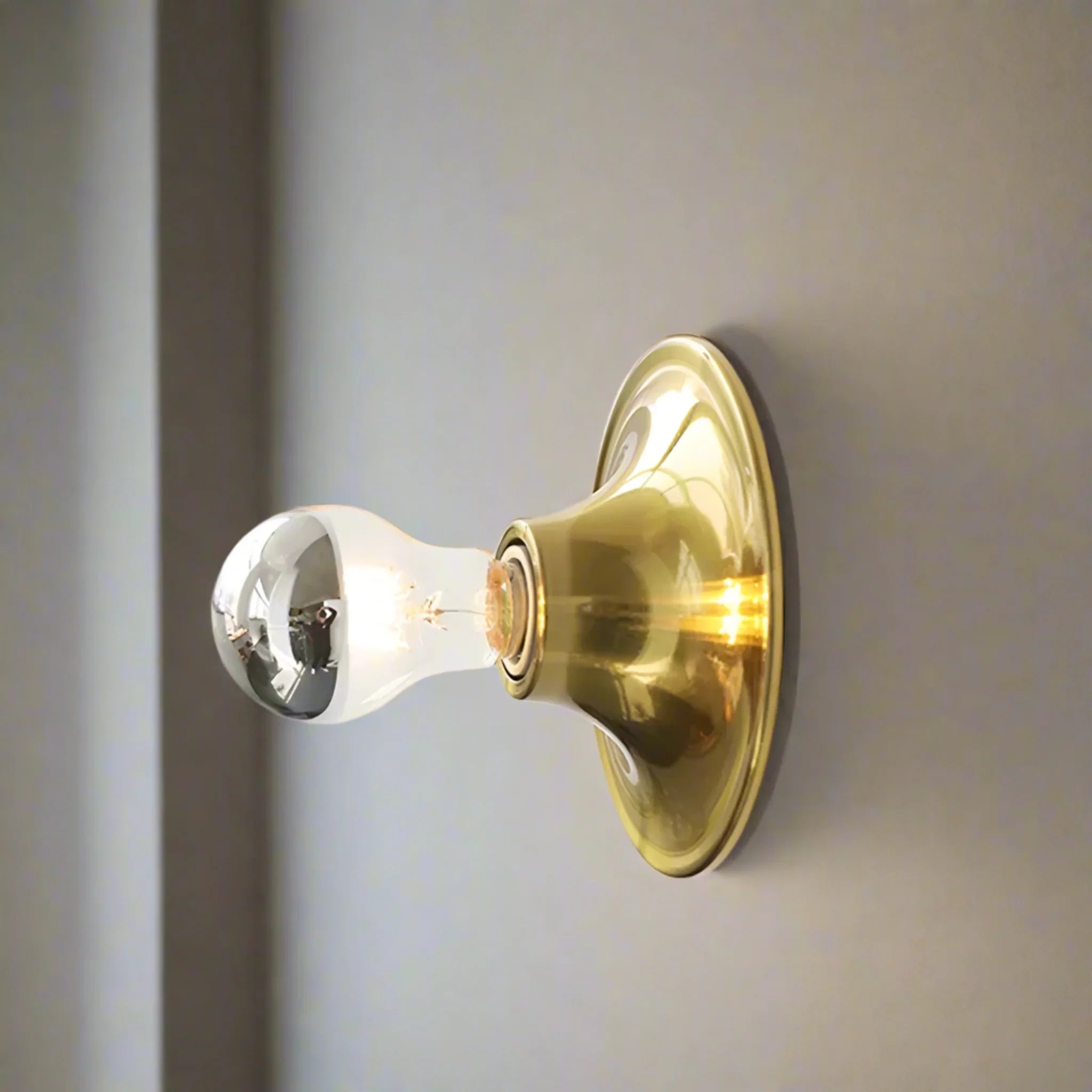 Gold wall sconce with a light bulb on a neutral background