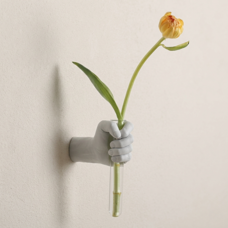 Wall-mounted vase shaped like a hand holding a yellow tulip against a beige background