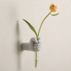 Wall-mounted vase shaped like a hand holding a yellow tulip against a beige background