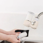Person cleaning a white cup under a running faucet with a beige water filter.