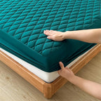 Person adjusting a teal mattress cover on a wooden bed frame.