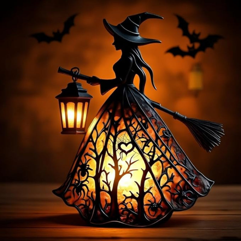 A Halloween decorative figurine shaped like a witch in a flowing dress, holding a glowing lantern. The dress has intricate cutout details of trees, spiders, and hearts, illuminated from within with a warm orange glow.