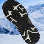 A close-up of a black and white winter hiking boot sole with aggressive tread, set against a blurred snowy mountain background.
