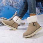 A person wearing beige ankle-height winter boots with white faux-fur cuffs and side zippers, standing in a snowy outdoor-style setting with a blue winter forest backdrop.