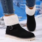 Black ankle winter boots with fluffy white faux-fur cuffs and a buckle strap, shown on a model standing in snow with a snowy forest backdrop.