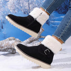 Black ankle winter boots with fluffy white faux-fur trim and a buckle detail, shown on a person wearing blue jeans in a snowy outdoor setting.