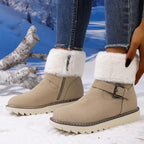 A pair of beige faux-suede ankle boots with white faux-fur trim and a buckle strap, shown on a model wearing blue jeans in a snowy outdoor setting.
