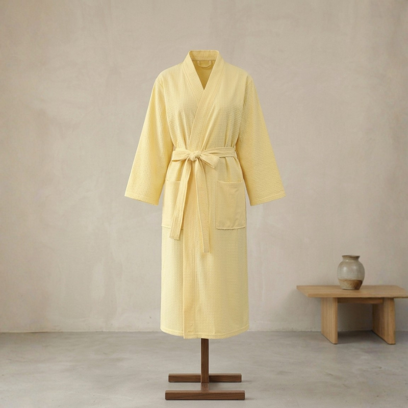 Yellow bathrobe on a mannequin against a beige wall with a wooden table and vase in the background.