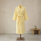 Yellow bathrobe on a mannequin against a beige wall with a wooden table and vase in the background.