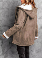 Person wearing a brown coat with white trim against a gray concrete wall.