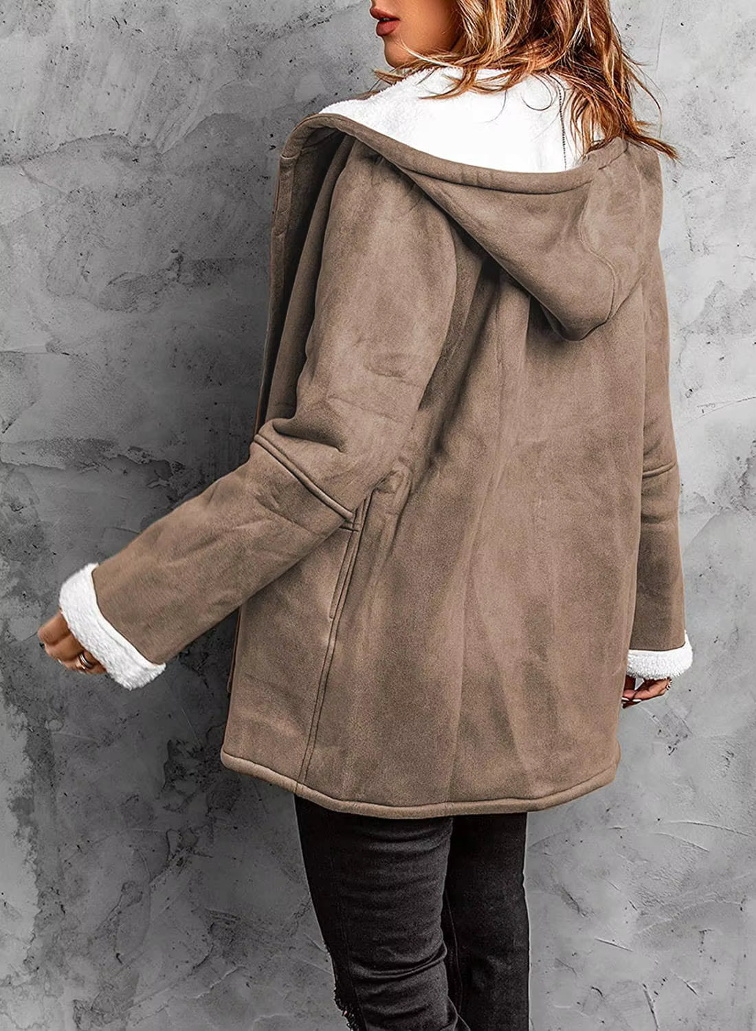 Person wearing a brown coat with white trim against a gray concrete wall.