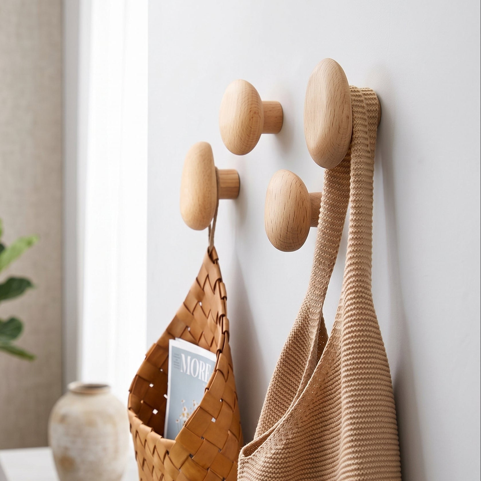 Wooden wall hooks with bags and a magazine on a white wall.