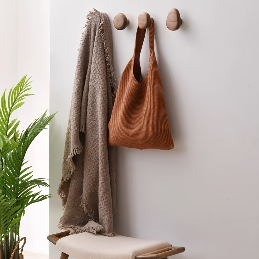 Brown bag and blanket hanging on wooden hooks against a white wall with a plant in the corner.