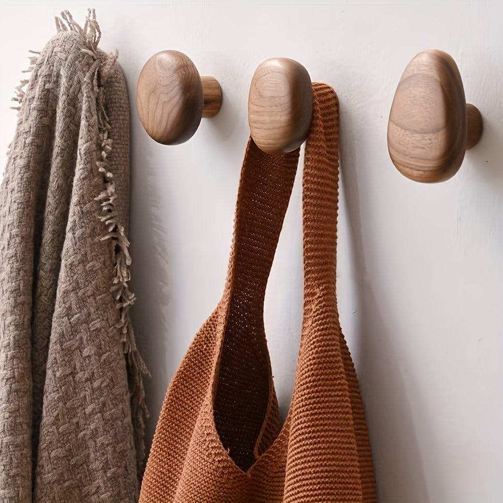 Wooden hooks on a white wall with a brown textured towel and a brown knitted bag.