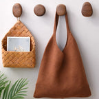Brown woven bag hanging on a wooden hook with a wall-mounted basket below.