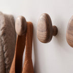 Wooden hooks on a white wall with a brown textured fabric.