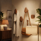Wooden wall hooks with a coat, bag, and lampshade on a neutral wall.