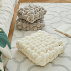 Two braided pillows, one beige and one white, on a textured surface.