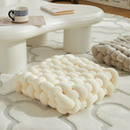 White woven ottoman on a textured rug with a coffee table in the background