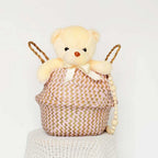 Plush teddy bear in a woven basket with wooden beads on a white background