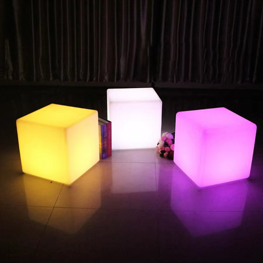 Three illuminated LED cubes in yellow, white, and pink on a dark floor.