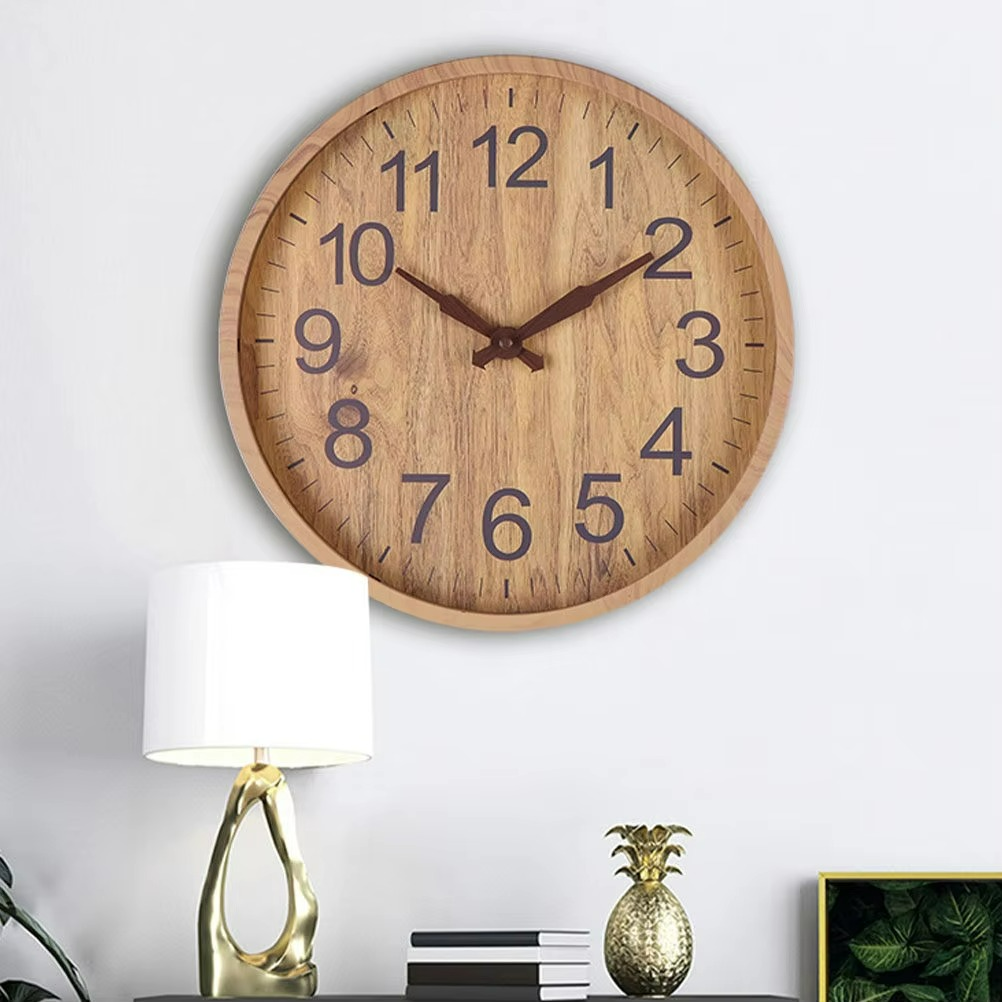 Wooden wall clock on a white wall with a lamp and decorative items below.