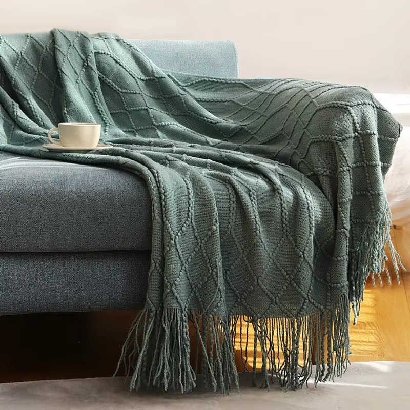 Green textured blanket draped over a gray sofa with a cup on a small table.