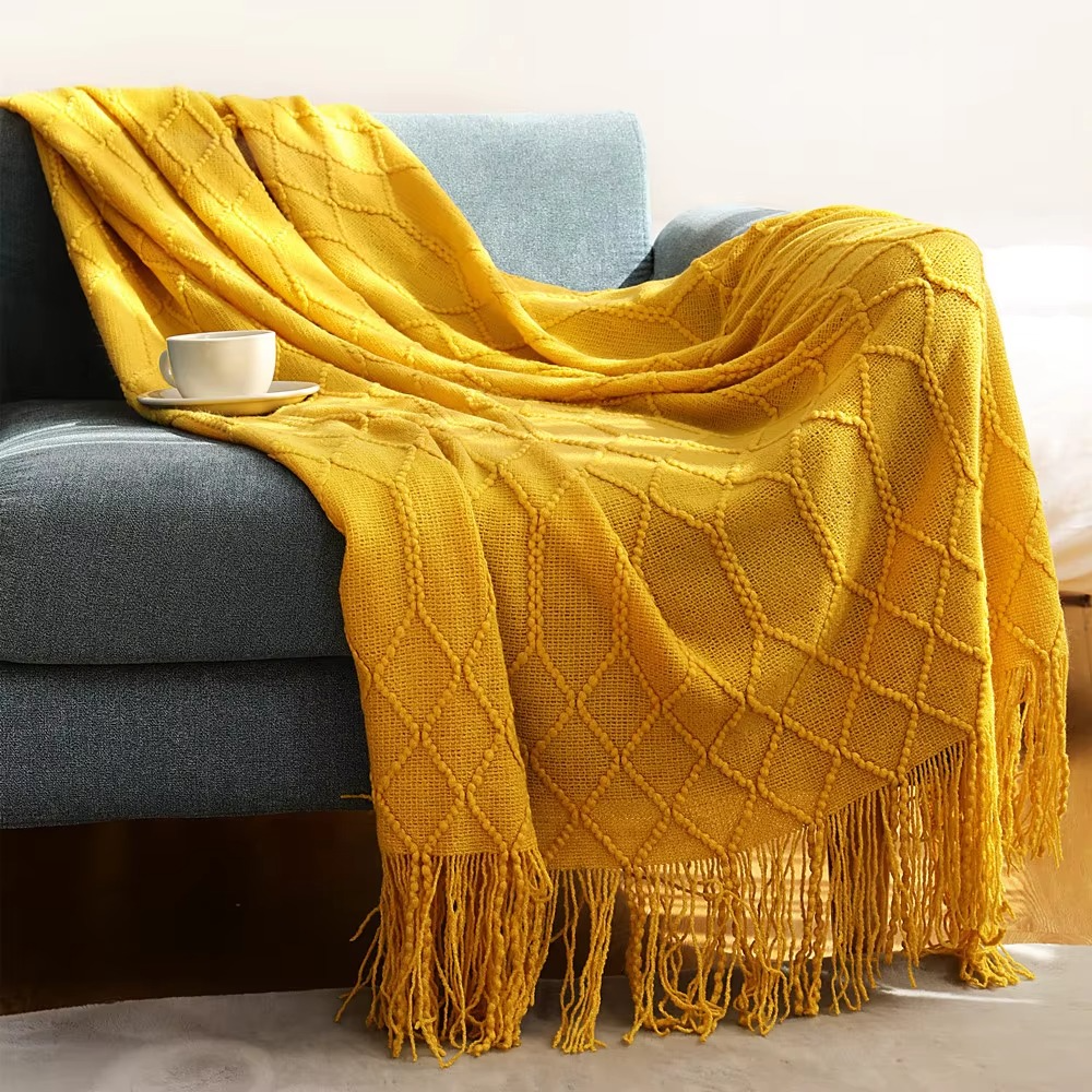 Yellow blanket with tassels draped over a gray sofa in a living room setting.