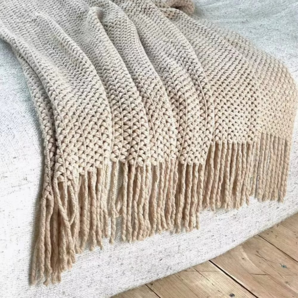 Beige knitted blanket with fringe on a light surface