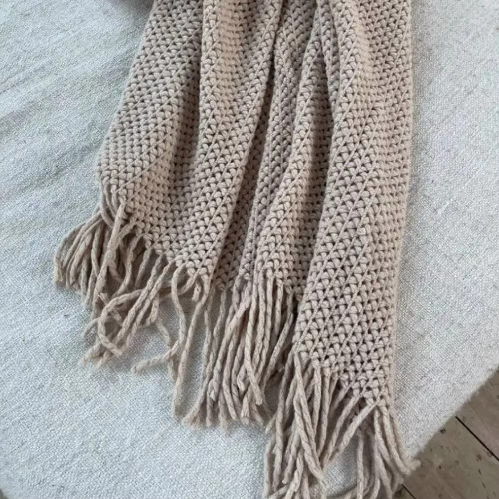 Beige knitted throw blanket with fringes on a light gray surface