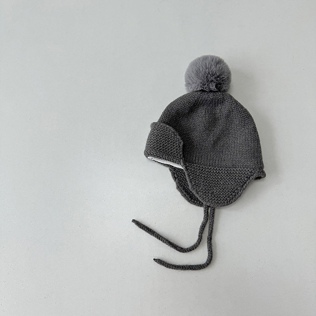 Gray knit baby hat with a pom-pom on a light gray background
