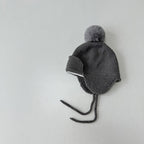 Gray knit baby hat with a pom-pom on a light gray background