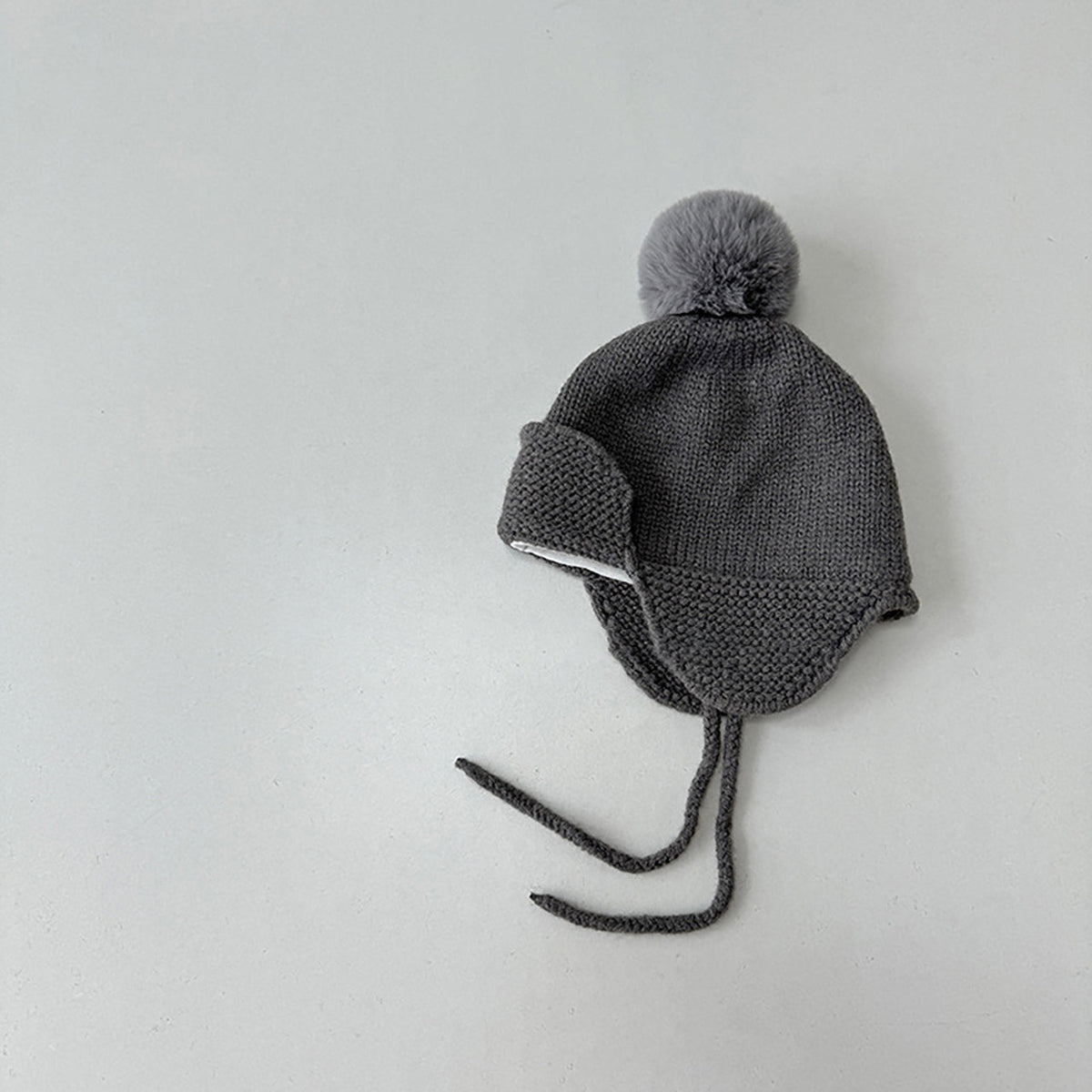Gray knit baby hat with a pom-pom on a light gray background