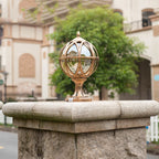 Decorative gold sphere on a stone pedestal with a blurred building and trees in the background