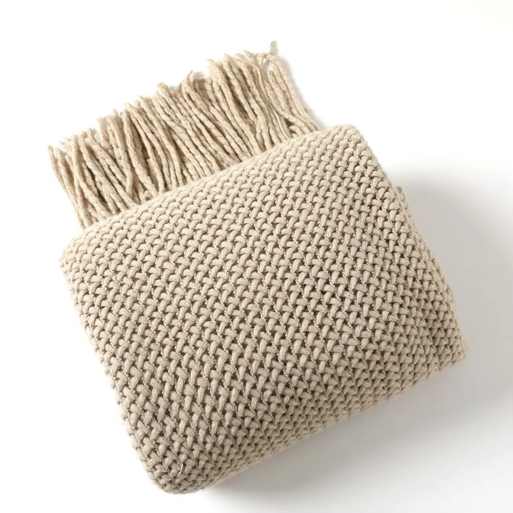 Beige knitted throw blanket with tassels on a white background