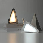 Two triangular table lamps on a gray surface with a neutral background