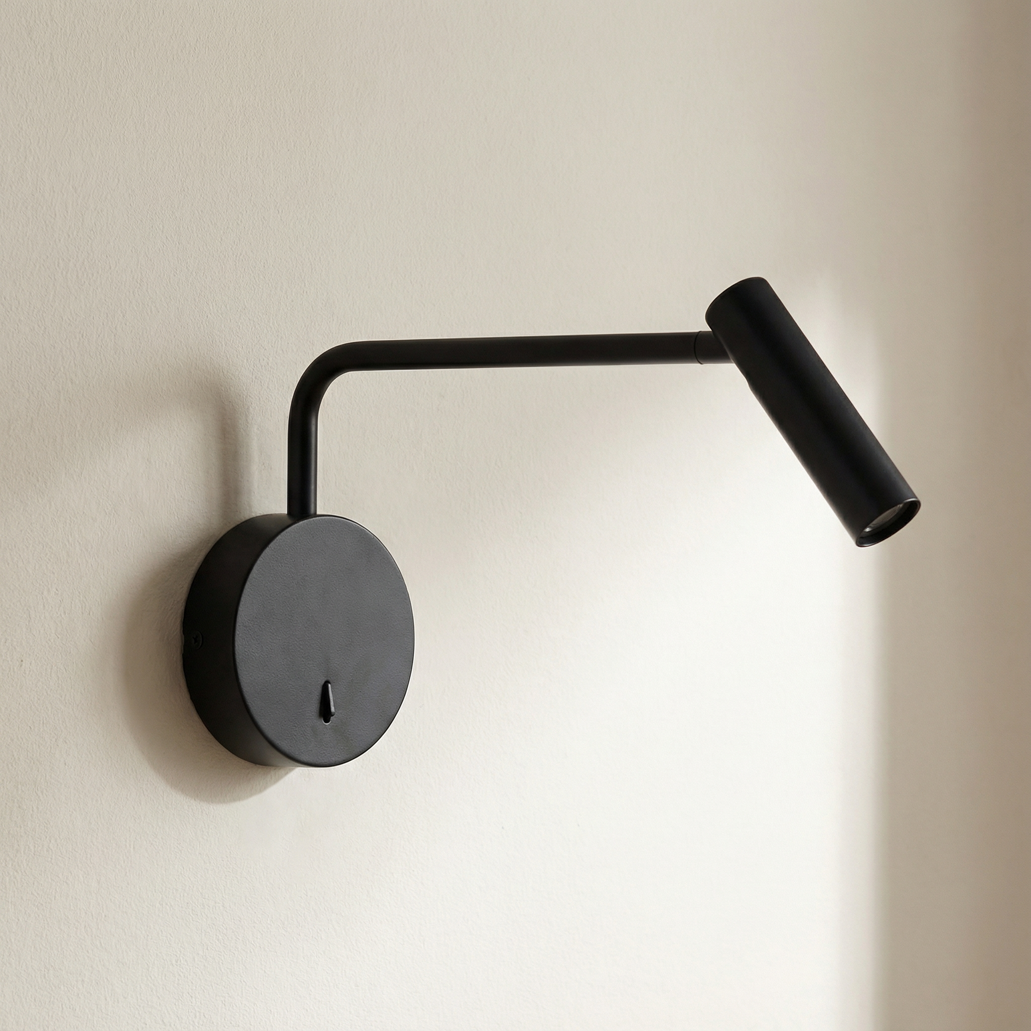 Black wall-mounted lamp with adjustable arm on a beige wall