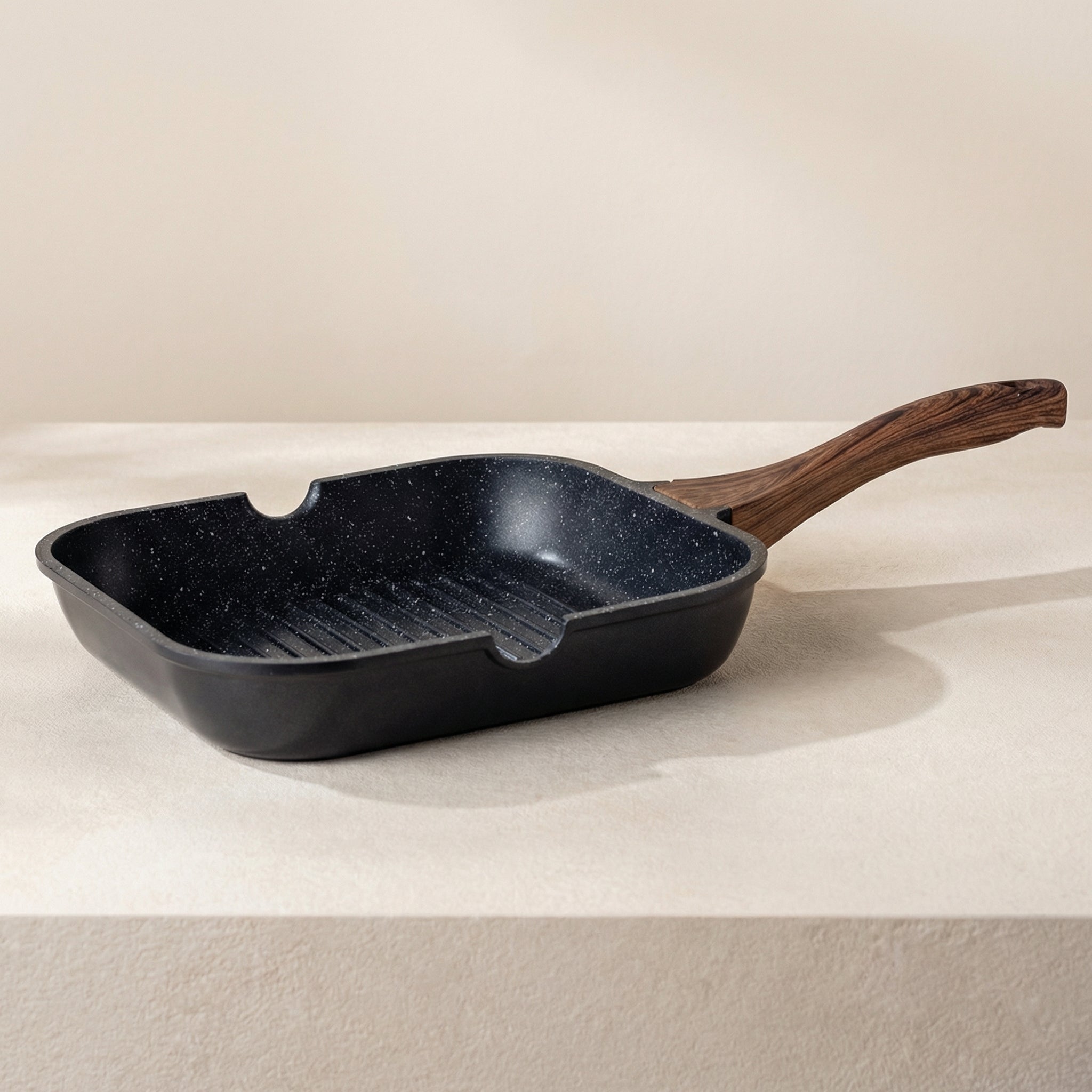 Black speckled cast iron skillet with wooden handle on a beige background