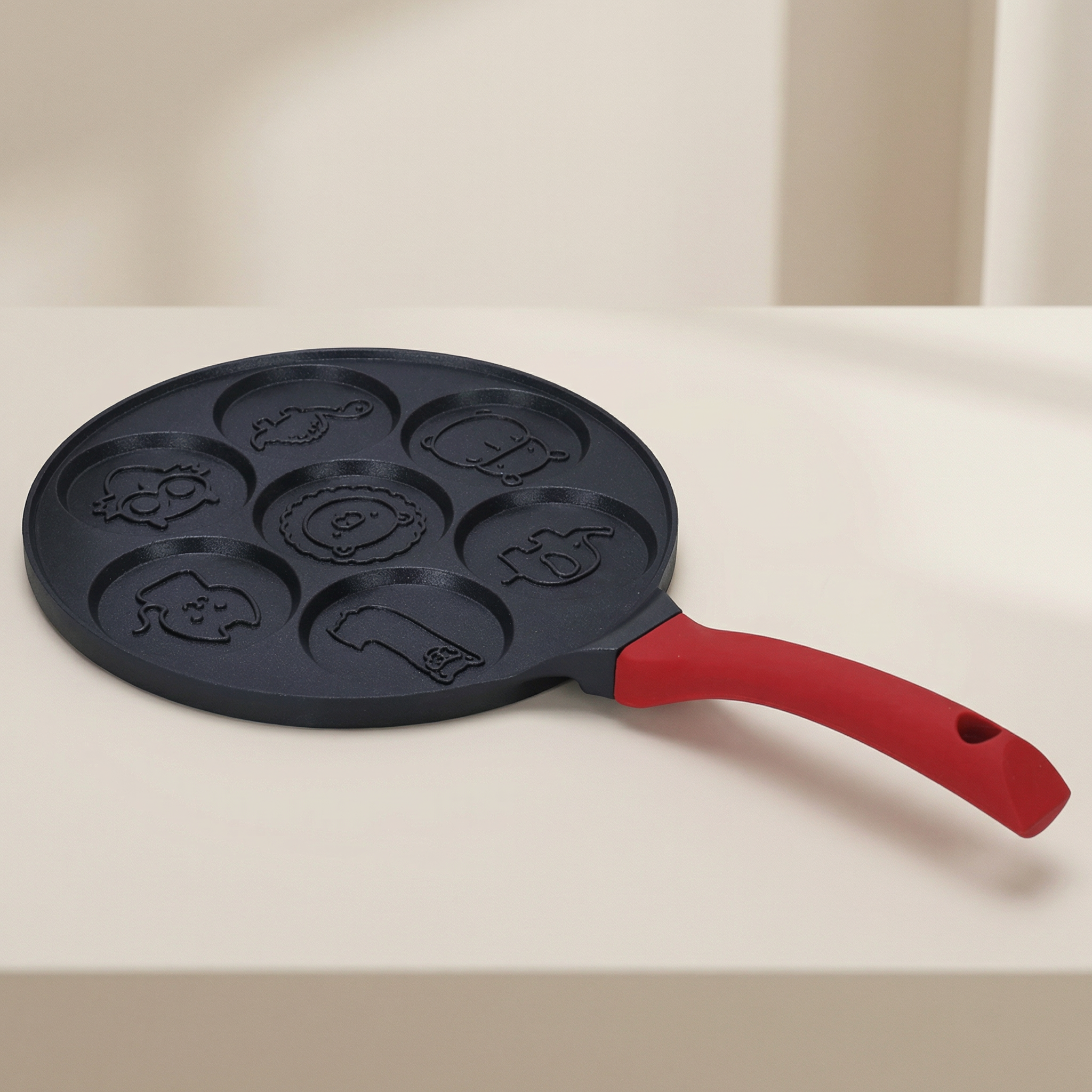 Black pan with cartoon character molds and red handle on a beige background