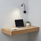 Wooden wall-mounted desk with a laptop, notebook, and plant against a light gray wall.