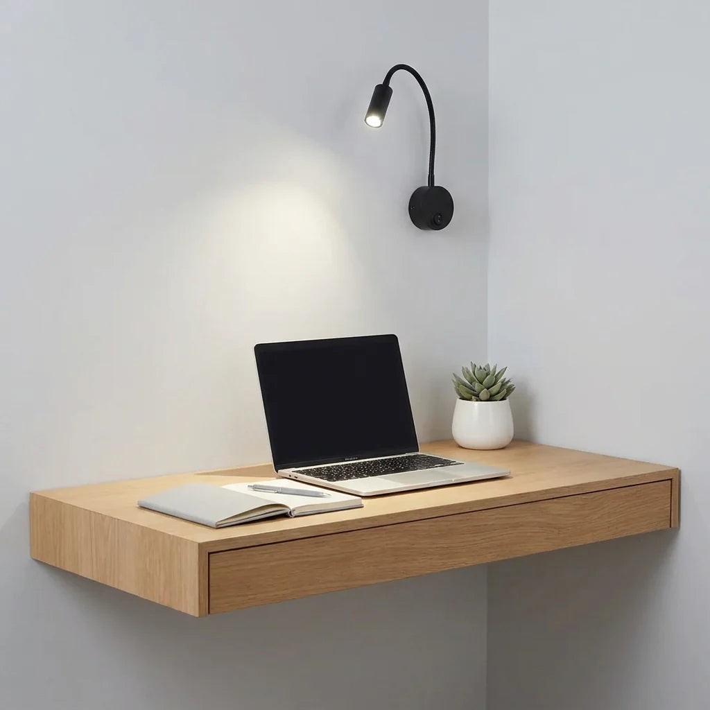 Wooden wall-mounted desk with a laptop, notebook, and plant against a light gray wall.